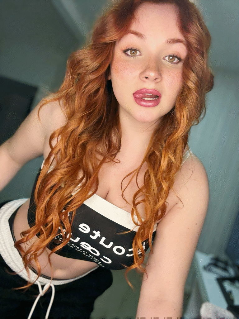 Sexy Redheads: A Beleza do Rutilismo. Mulher ruiva com longos cabelos ondulados e olhos claros, exibindo sardas e uma pose sedutora. Veste um top cropped preto e branco. Imagem de beleza natural e estilo casual.