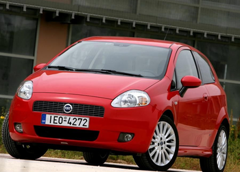 Fotografia em plano frontal de um carro Fiat Grande Punto vermelho, estacionado ao ar livre em um dia claro.