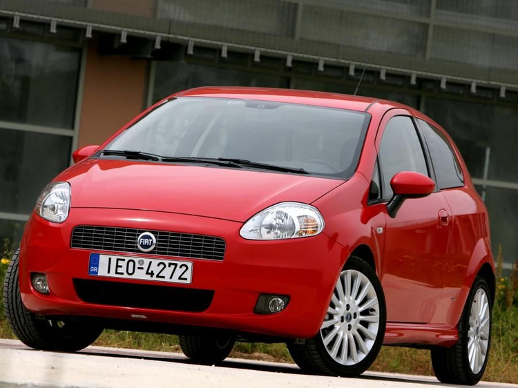 Fotografia em plano frontal de um carro Fiat Grande Punto vermelho, estacionado ao ar livre em um dia claro.